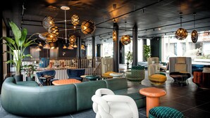 Un espace de détente moderne avec un canapé vert aux lignes courbes, différents types de sièges et des luminaires sphériques suspendus.
