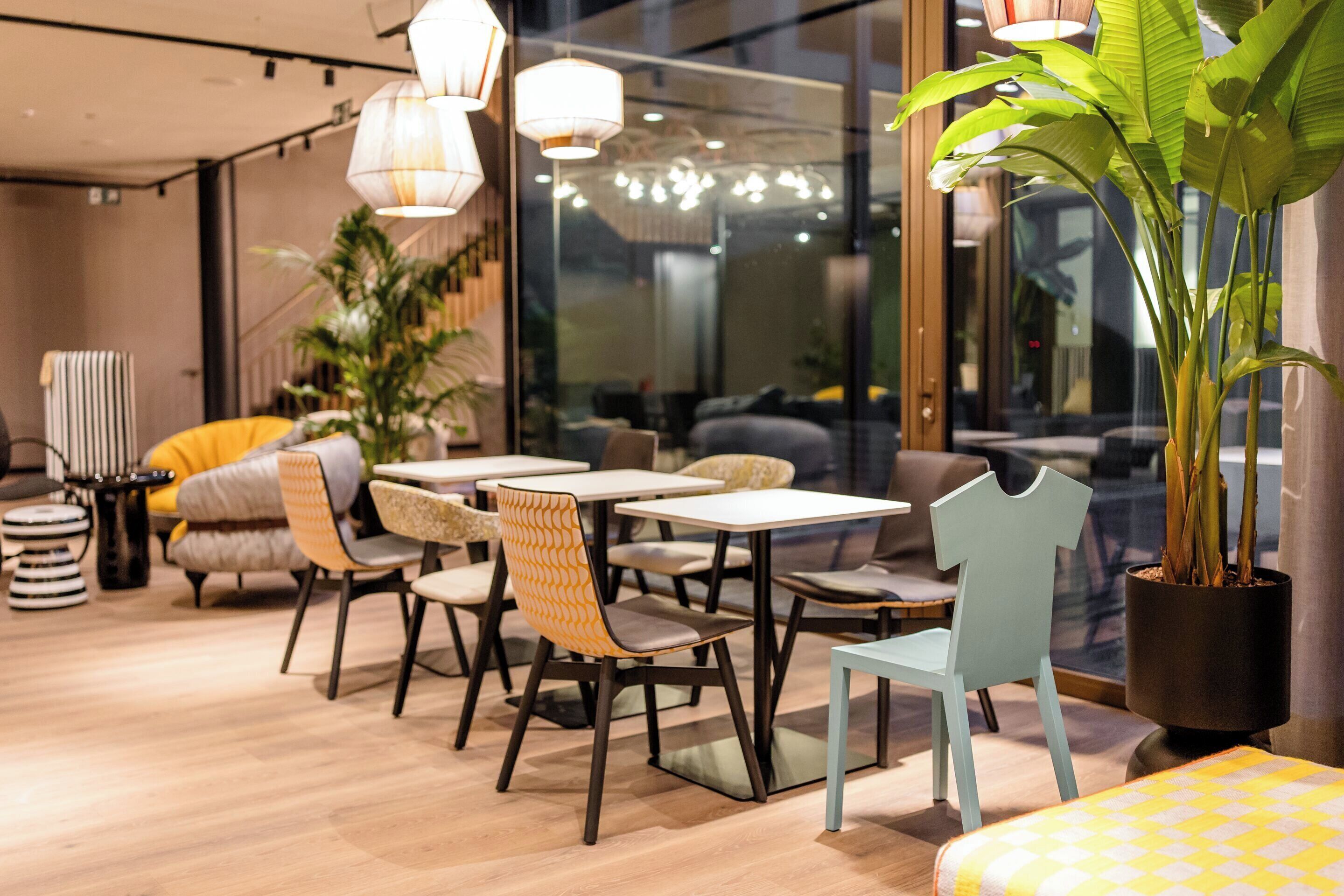 A modern cafe with tables and chairs, a large potted plant, and hanging lights.