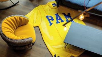 Uma camisa esportiva amarela com a inscrição "PAM", uma poltrona acolchoada amarela e um chão de madeira.