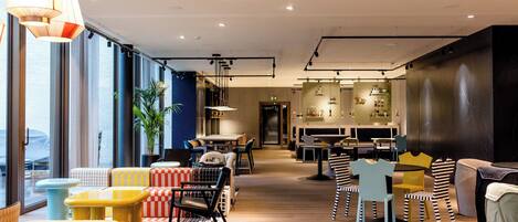 A modern interior with a mix of seating areas, including colorful chairs and tables, and a bar area with stools.