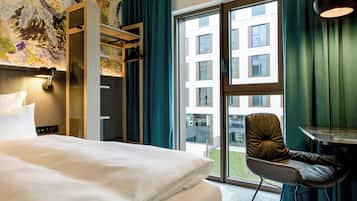Habitación de hotel con una cama grande, una silla, una mesa y vistas a un edificio a través de un ventanal.