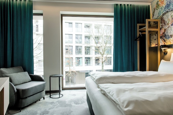 A hotel room with a bed, a sofa, a small table, and a large window with curtains.