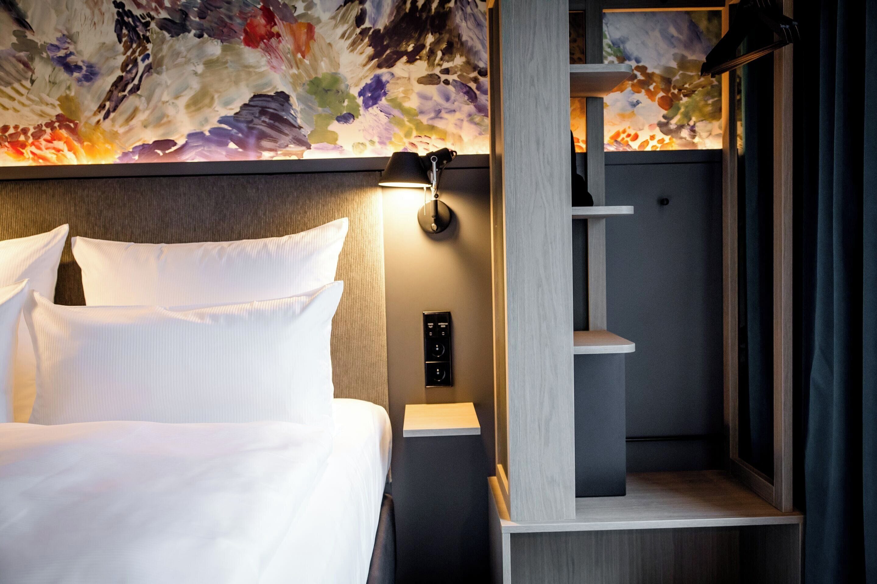 A hotel room with a bed, a nightstand, a wall-mounted lamp, and a shower area.