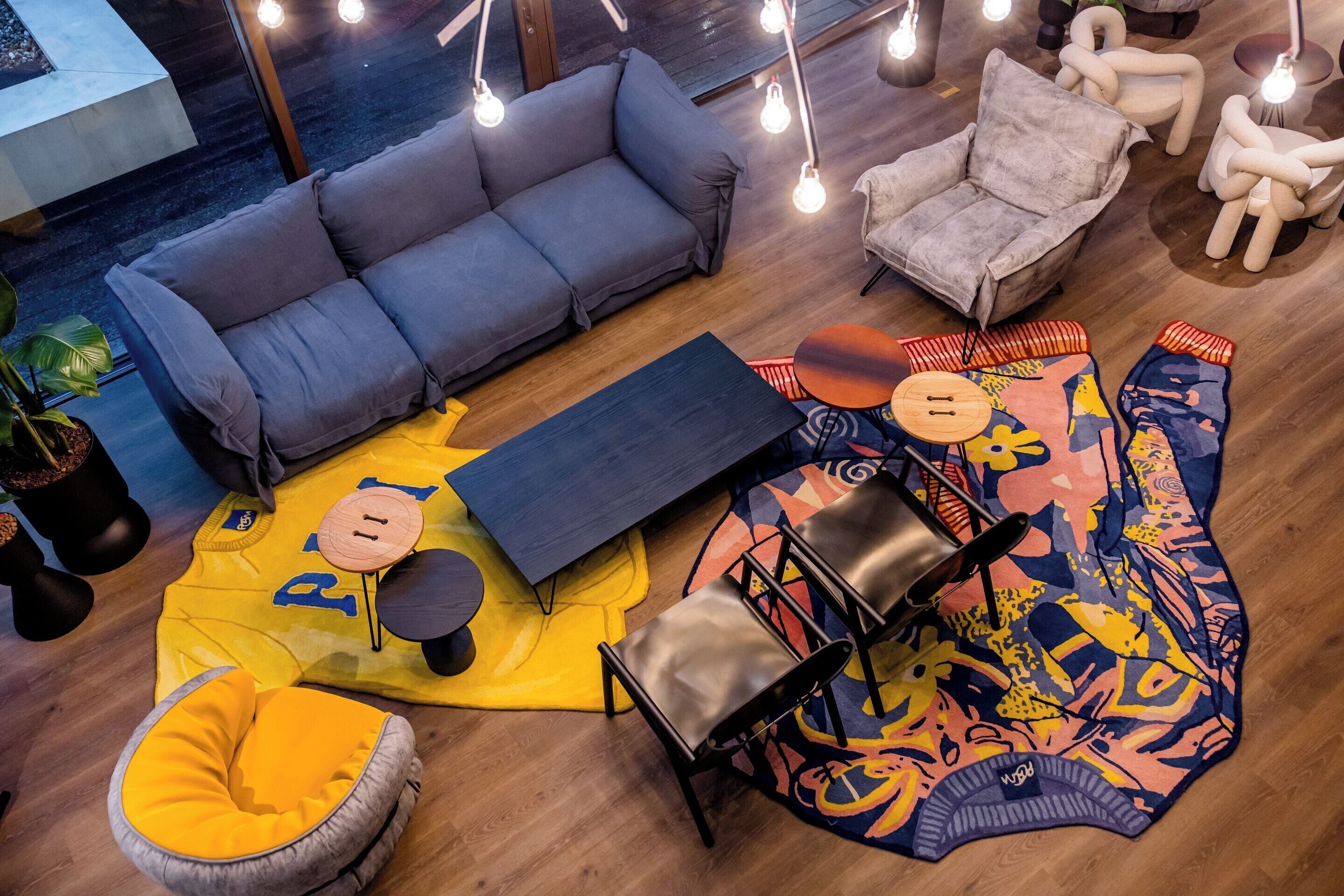Un salon moderne avec un canapé gris, un tapis jaune et un tapis abstrait aux couleurs vives. On y trouve deux fauteuils et une petite table.