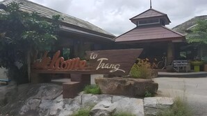 A wooden sign with 'Welcome to Trang' written on it, placed in front of a building with a tiled roof and a small tower-like structure on top. - Khaopubpa Resort (Na Yong)