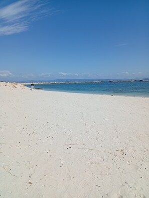A beach with white sand, a rocky breakwater, and a clear blue sky.