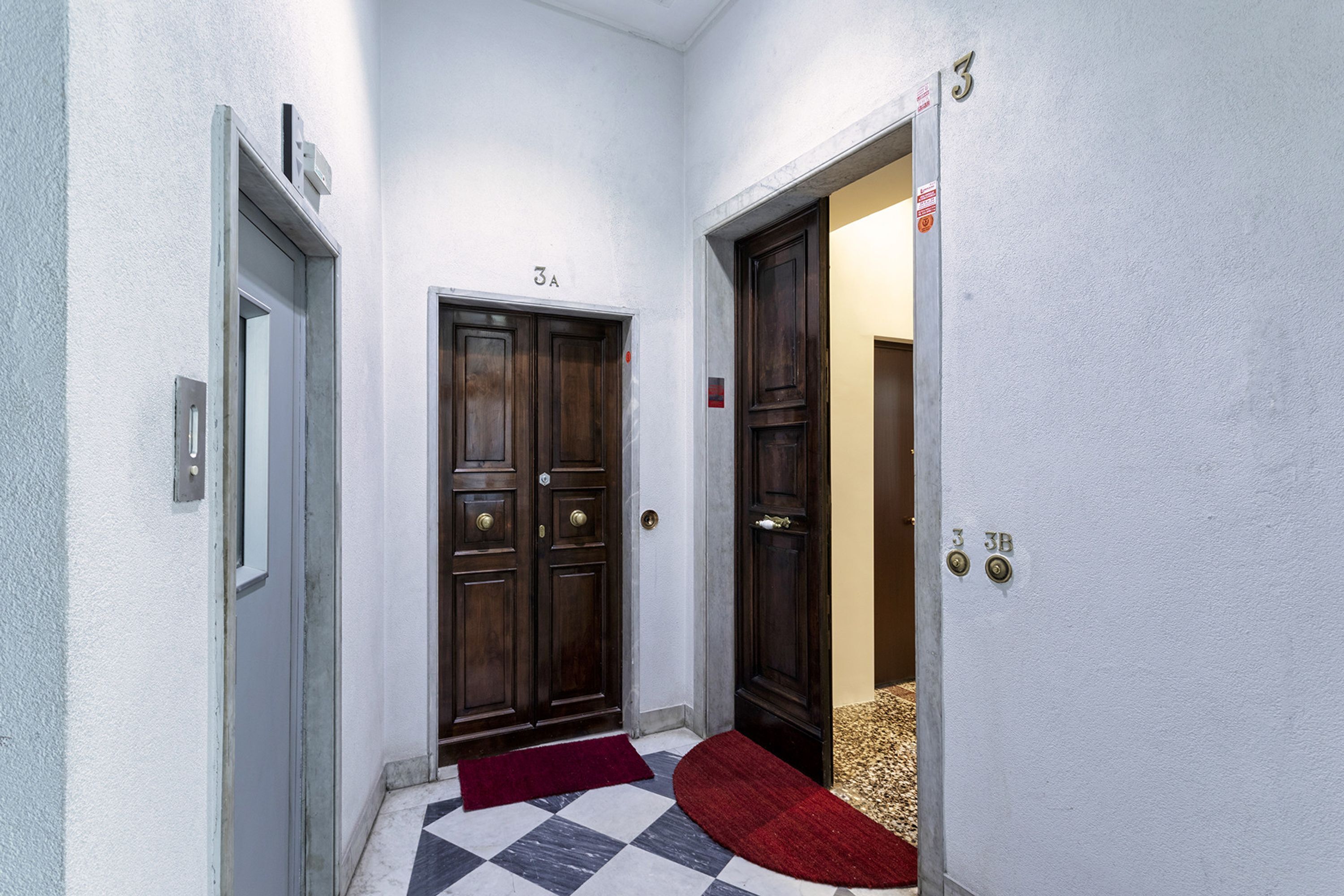 Un couloir avec deux portes en bois, une moquette rouge et un sol à carreaux.