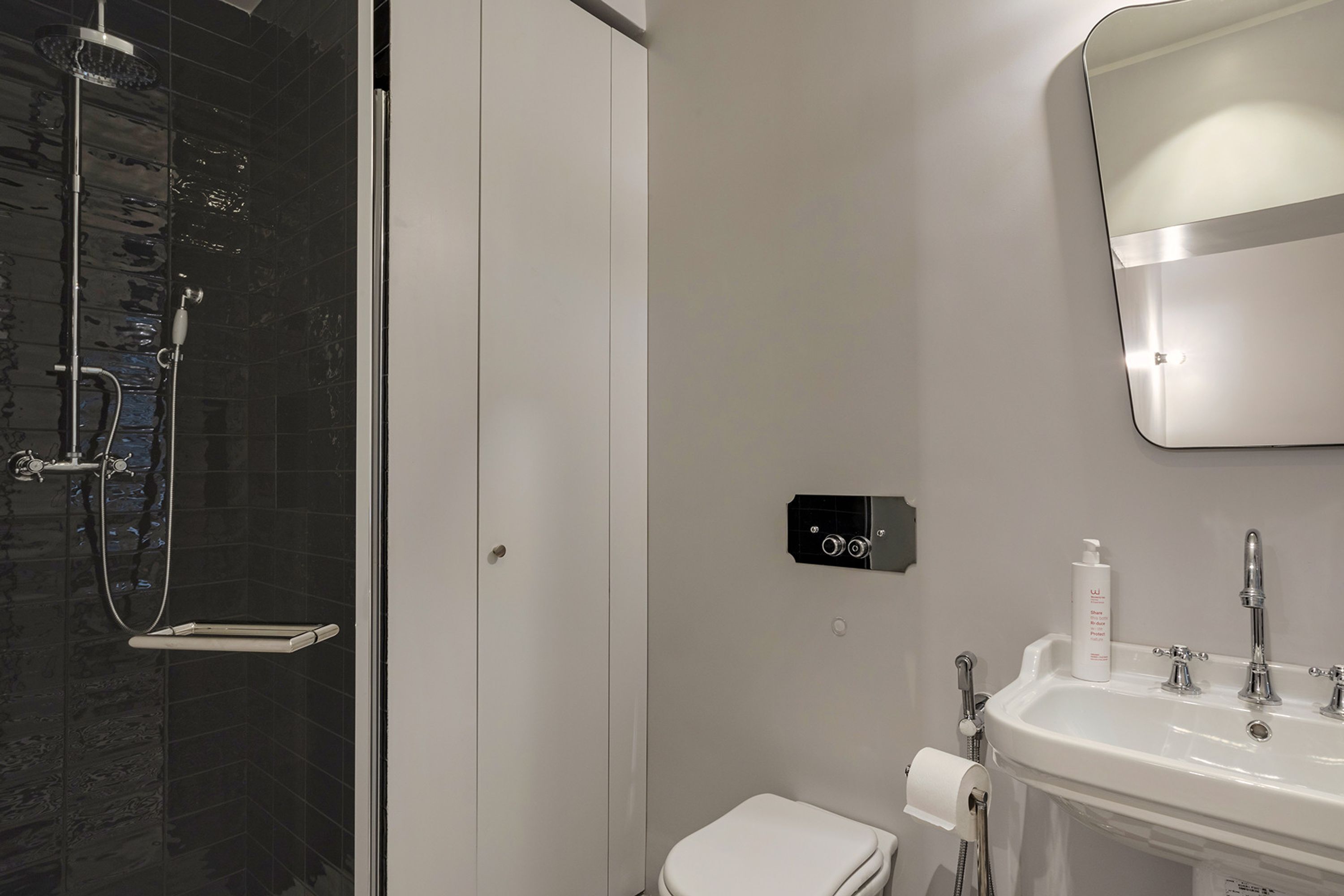Et moderne badeværelse med brusekabine i glas, hvidt toilet, vask med spejl og et kontrolpanel.
