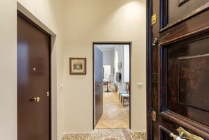 Un pasillo con una puerta de madera a la izquierda, un cuadro en la pared y vista a una habitación con una mesa y sillas de comedor.