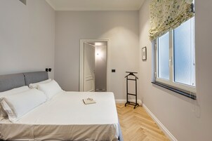 Un dormitorio con cama, ventana con cortina, una puerta y una mesita.