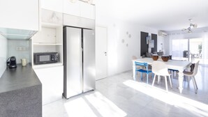 Une cuisine moderne avec des meubles blancs, un four à micro-ondes encastré et un réfrigérateur. On y trouve également un coin repas avec une table et des chaises blanches.