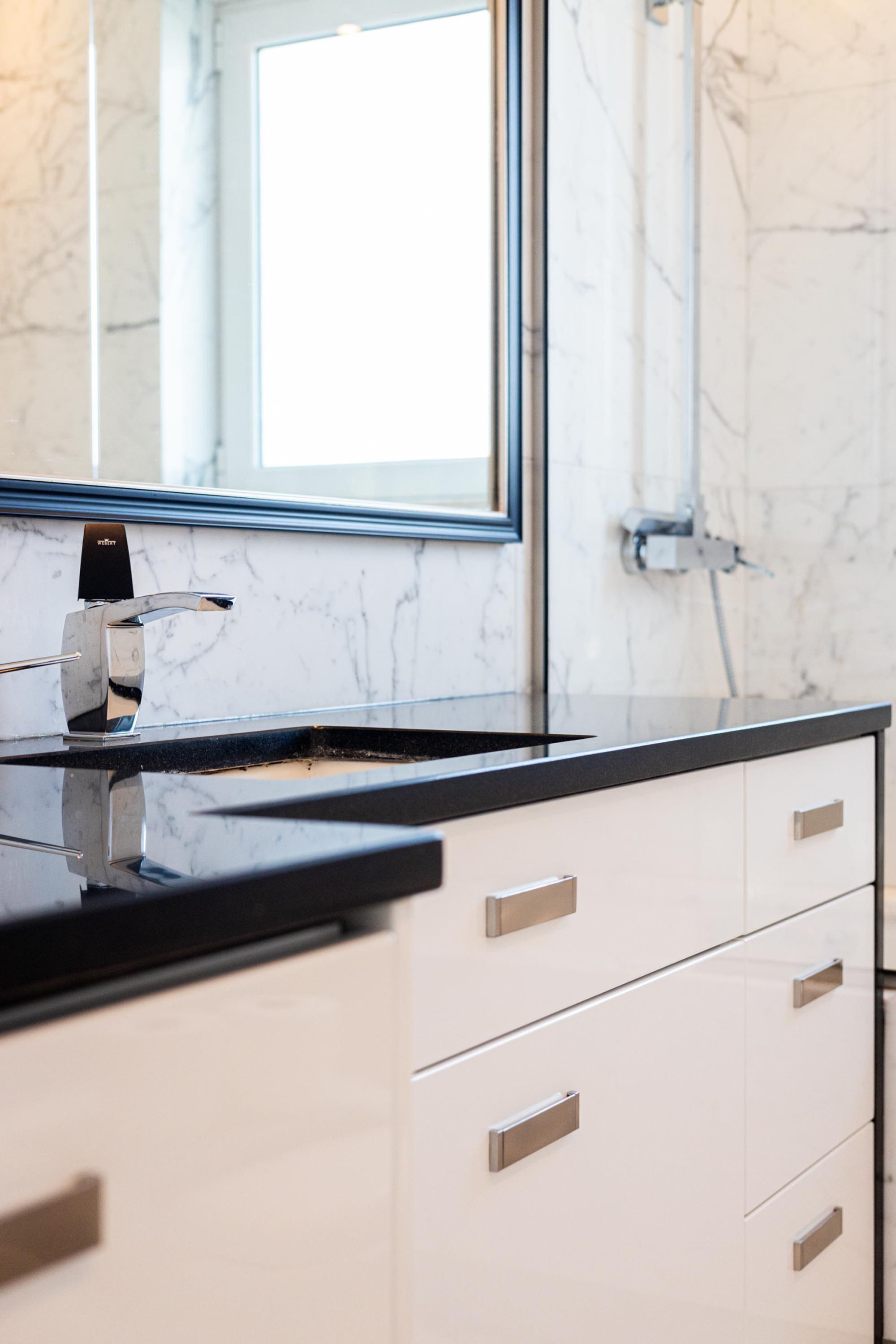 A modern bathroom with a black countertop, a chrome faucet, and a large mirror.