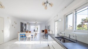 Une cuisine moderne dotée d’un grand îlot central, d’un coin repas avec une table et des chaises, et offrant une vue sur l’extérieur grâce à de grandes fenêtres.