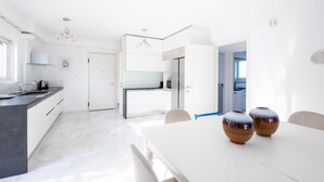 Une cuisine moderne avec des meubles blancs, un îlot central et un coin repas comprenant une table et des chaises blanches.