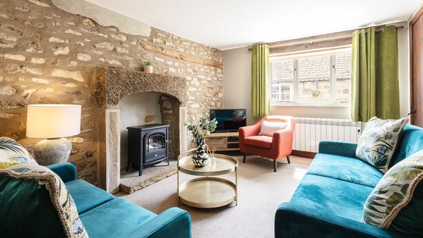 A cozy living room with a stone wall, a fireplace, a television, and a sofa. - Host Stay Heather Cottage (York)