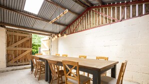 A rustic dining area with a long wooden table and chairs, a corrugated metal ceiling, and a wooden staircase. - Host Stay Heather Cottage (York)