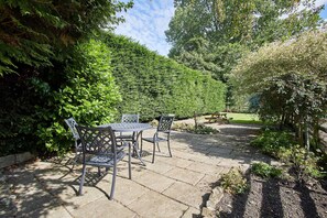 A patio with a table and chairs, surrounded by a hedge and trees. - Host Stay Heather Cottage (York)
