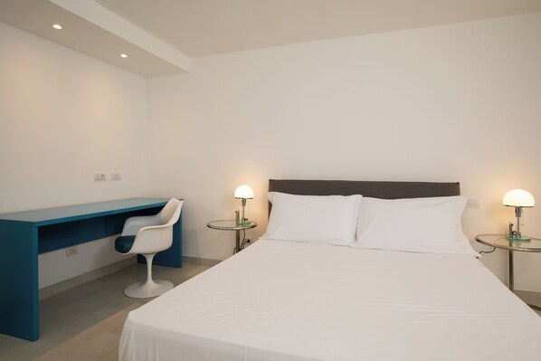 Una habitación de hotel con cama, escritorio, silla y dos lámparas de noche.
