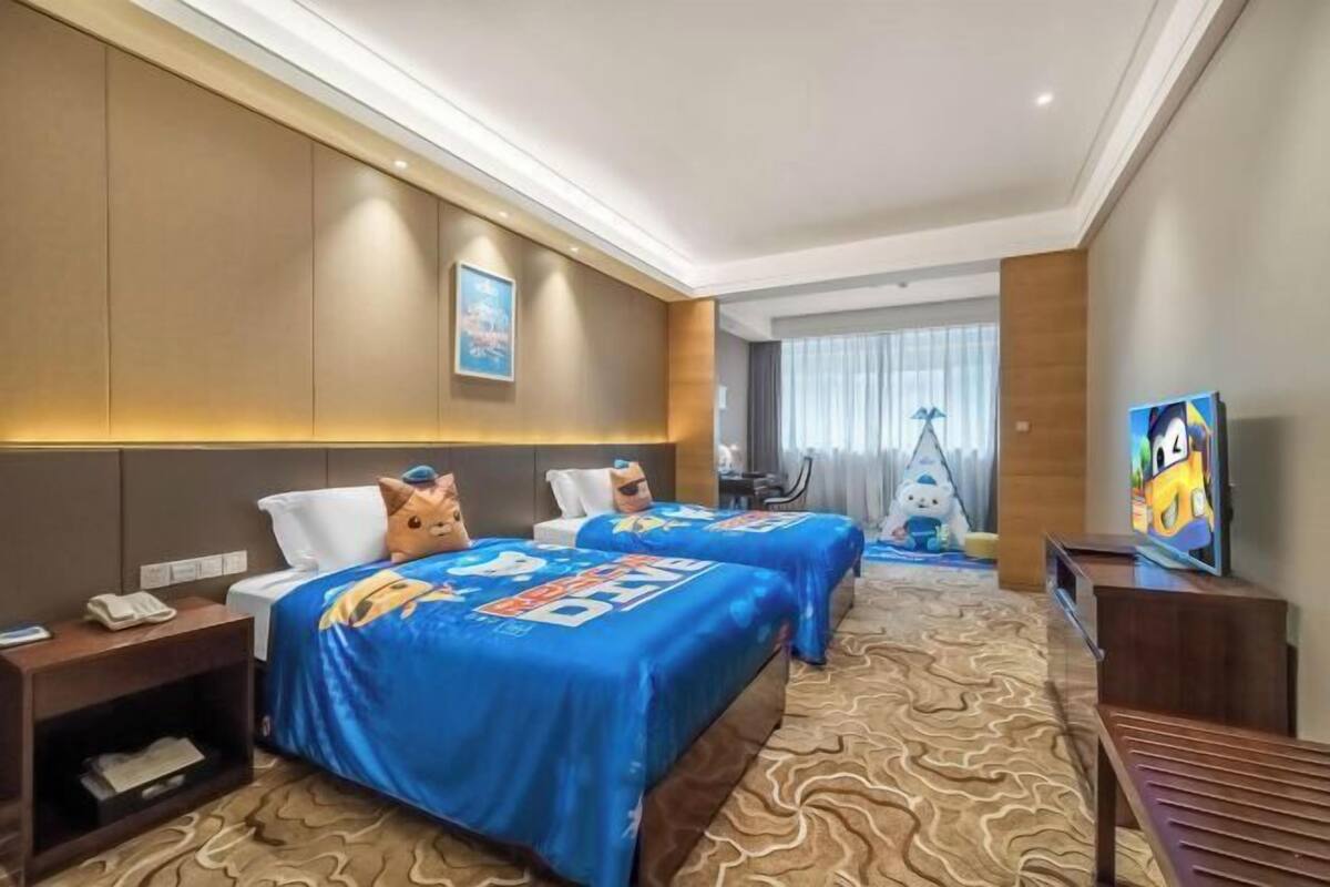A hotel room with two beds, a TV, a desk, and a view of the cityscape.