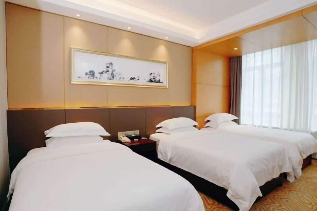 A hotel room with two beds, a nightstand with a phone, a framed artwork on the wall, and a window with curtains.