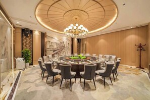 A conference room with a round table, chairs, a chandelier, and a view of a building through a window. - Chinese Entrepreneur International Conference Center (Chongqing)
