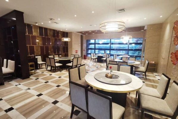A hotel lobby with multiple dining tables, chairs, a chandelier, and a large window with a view.