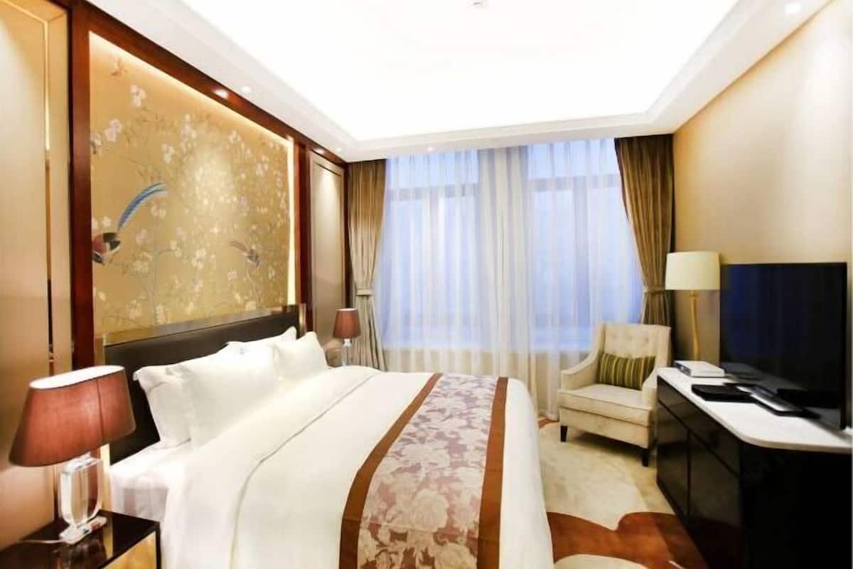 A hotel room with a large bed, a desk, a chair, and a television.