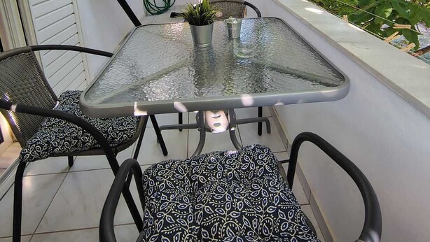 A glass-top table with two chairs, a potted plant, and a glass on the table. - Grandma’s Pine Apartments – Cozy Double Bed (Paralia Politikon)