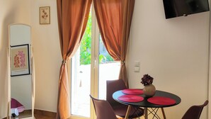 A room with a dining table, purple chairs, a flat-screen TV, and a window with curtains. - Grandma’s Pine Apartments – Cozy Double Bed (Paralia Politikon)