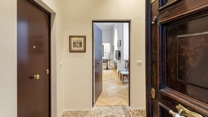 A hallway with a wooden door on the left, a framed picture on the wall, and a view into a dining area with a table and chairs. - Corvetto Luxury Suite by Wonderful Italy (Genova)
