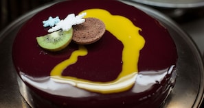 A dessert with a glossy surface, a slice of kiwi, a chocolate piece, and a dollop of cream on top.