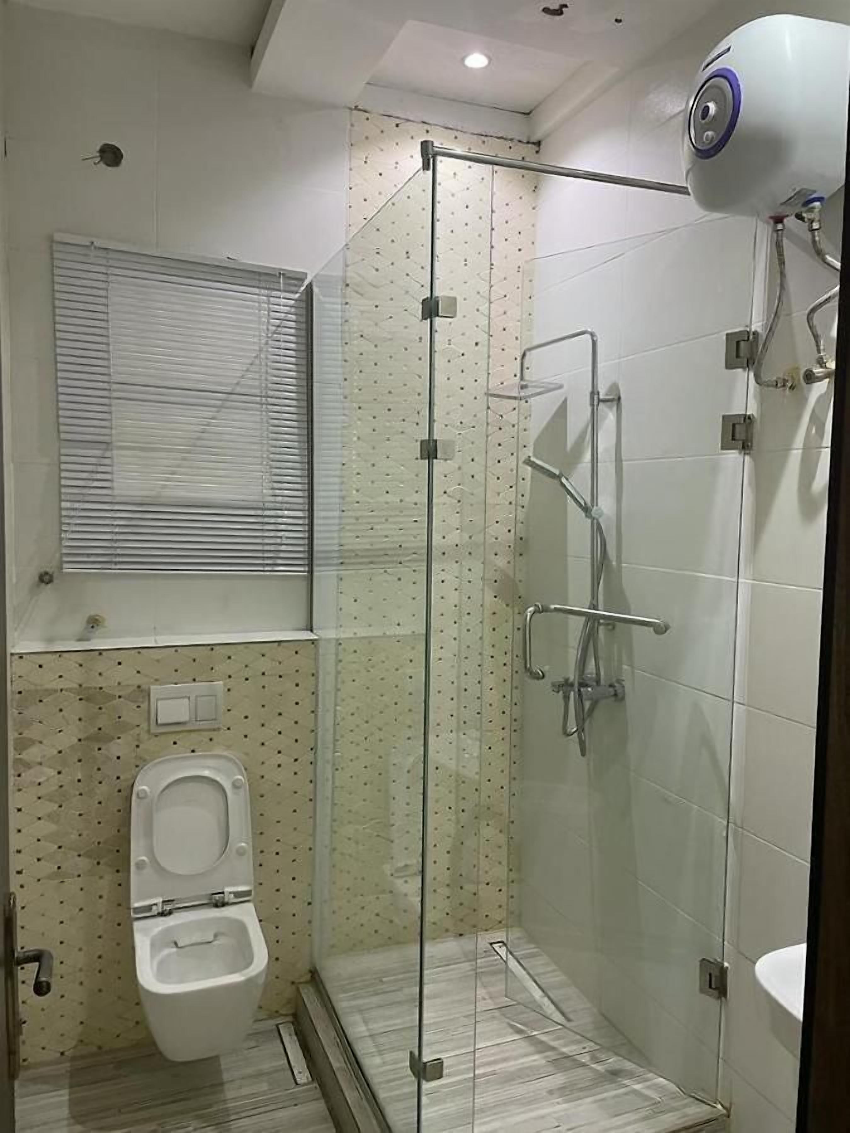 A modern bathroom with a glass-enclosed shower, a toilet, and a window.