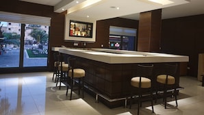 A modern bar area with a high counter, bar stools, and a display of bottles.