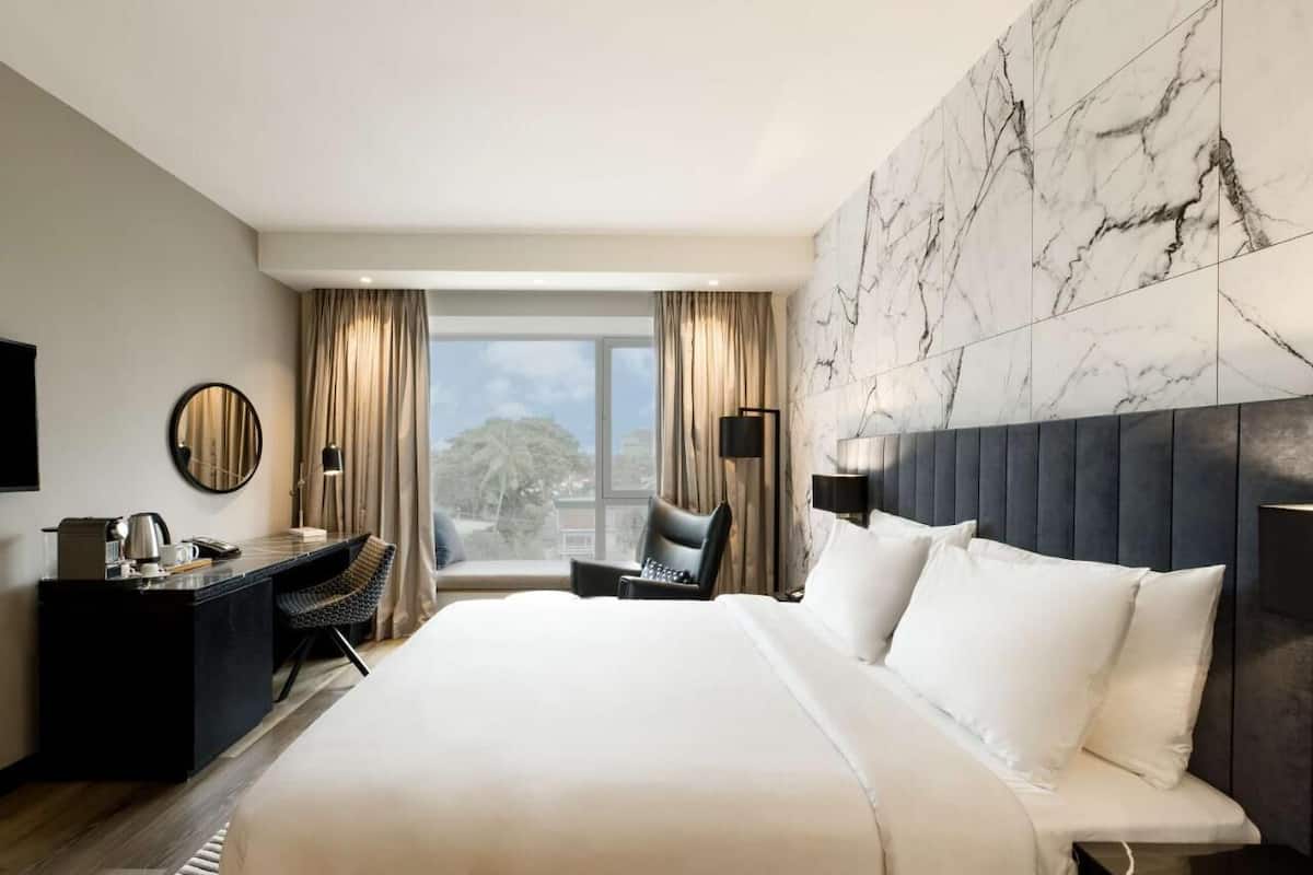 A modern hotel room with a large bed, a desk, a chair, and a view of the city.