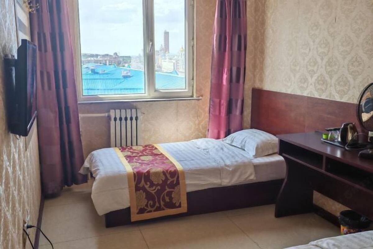 Una habitación con cama, escritorio, ventana y vistas a un paisaje urbano, además de un radiador.
