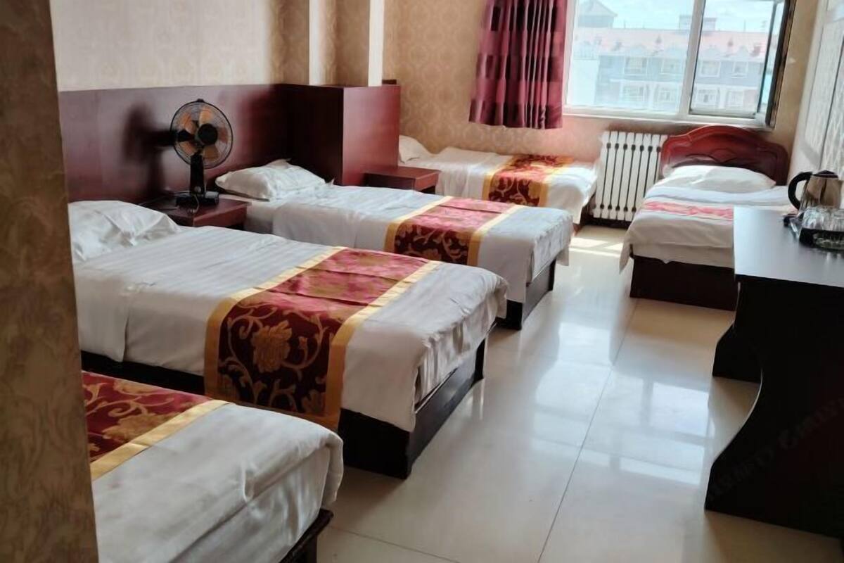 Habitación de hotel con cuatro camas, un escritorio, un ventilador y una ventana con cortinas.