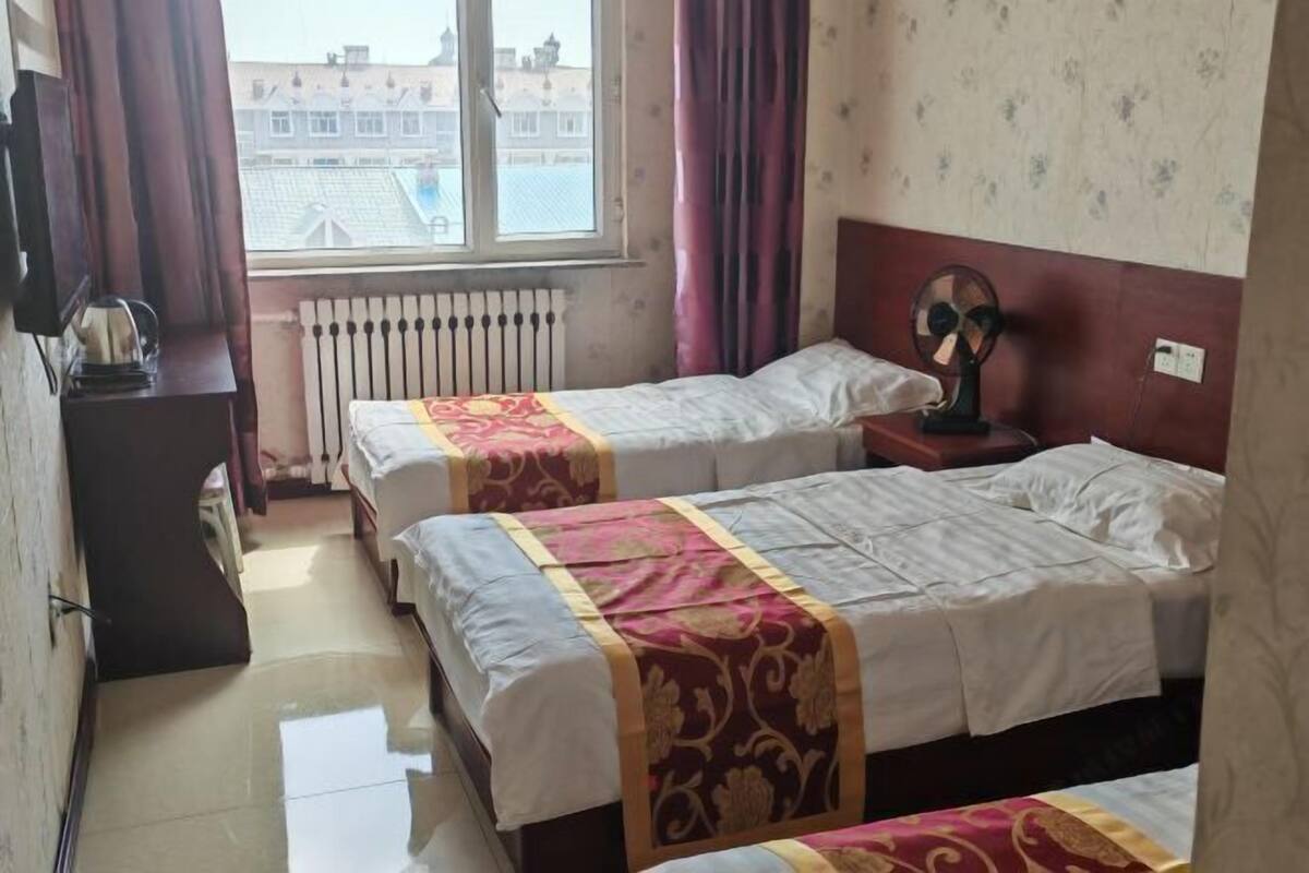Habitación de hotel con dos camas, un radiador, una ventana con cortinas, un ventilador y vistas a edificios.