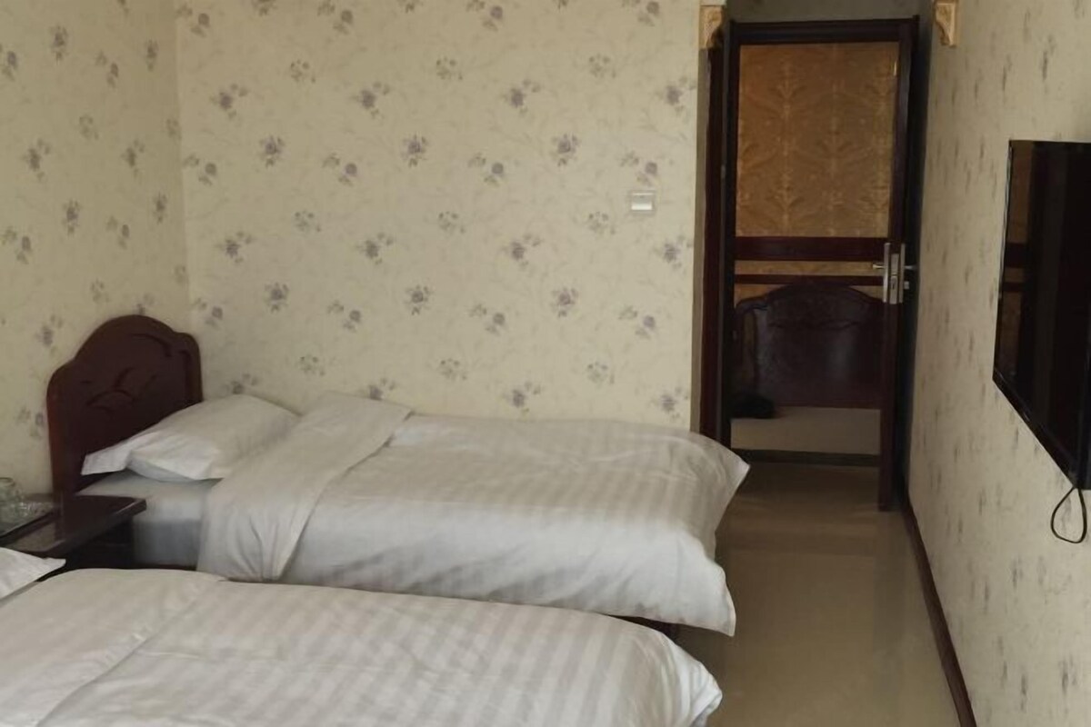 Ein Hotelzimmer mit zwei Betten, einem Holzkopfstück, einem an der Wand befestigten Fernseher und einer Tür zum Badezimmer.