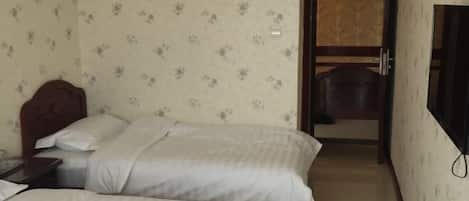 Habitación de hotel con dos camas, cabecero de madera, televisor en la pared y puerta que da a un baño.
