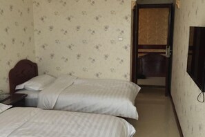 Ein Hotelzimmer mit zwei Betten, einem Holzkopfstück, einem an der Wand befestigten Fernseher und einer Tür zum Badezimmer.