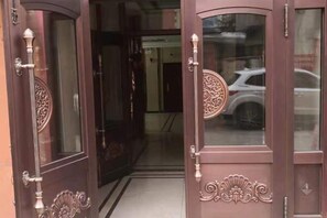 Une porte en bois ornée de sculptures complexes et d’un panneau de verre qui reflète une voiture blanche.