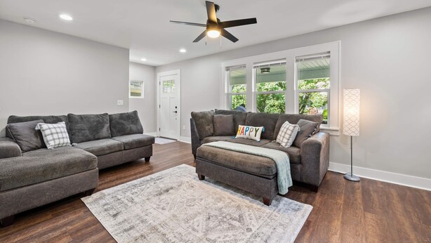 A modern living room with two grey sofas, a patterned rug, a ceiling fan, and a floor lamp.