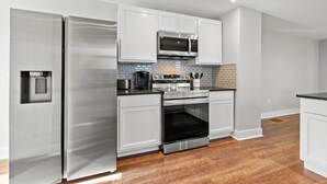 A modern kitchen with stainless steel appliances, white cabinetry, and a brick backsplash.