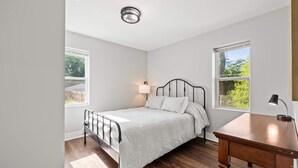 A bedroom with a bed, a desk, and two windows.