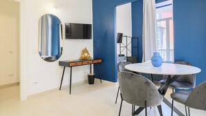 Un espace repas moderne avec une table ronde, des chaises grises, un vase bleu et un téléviseur fixé au mur.