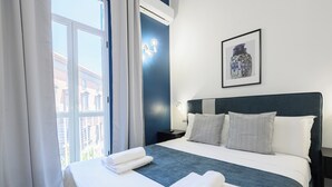 Une chambre d’hôtel avec un grand lit, du linge de lit blanc, une tête de lit sombre et un tableau encadré au mur.
