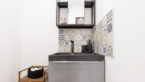 Een compacte keuken met een roestvrijstalen koelkast, een zwarte koffiezetapparaat en een decoratieve spatwand.