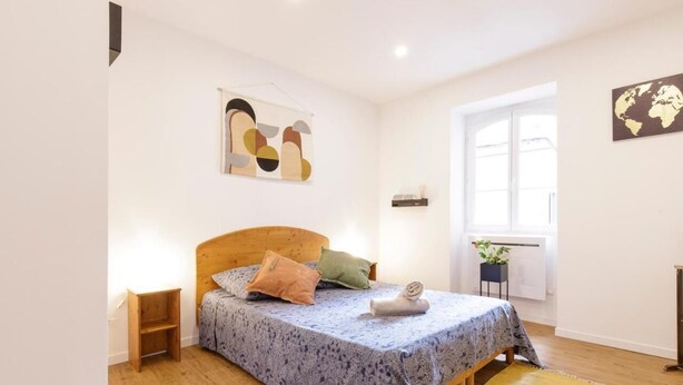 Een slaapkamer met een houten bed, een klein nachtkastje, abstracte kunst aan de muur, een raam met uitzicht, en een wereldkaart.