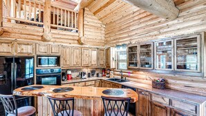 A spacious kitchen with wooden cabinets, a large island with bar stools, and a high ceiling with exposed beams. - Naffcation Lodge OKC Cabin And Guest House Retreat On 5 Acres (Oklahoma City)