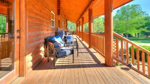 A wooden log cabin with a covered porch, furnished with outdoor seating and a view of the surrounding forest. - Naffcation Lodge OKC Cabin And Guest House Retreat On 5 Acres (Oklahoma City)